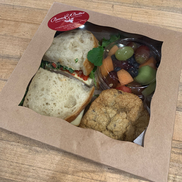 Packaged meal with sandwich, cookies, and fruit on a wooden surface